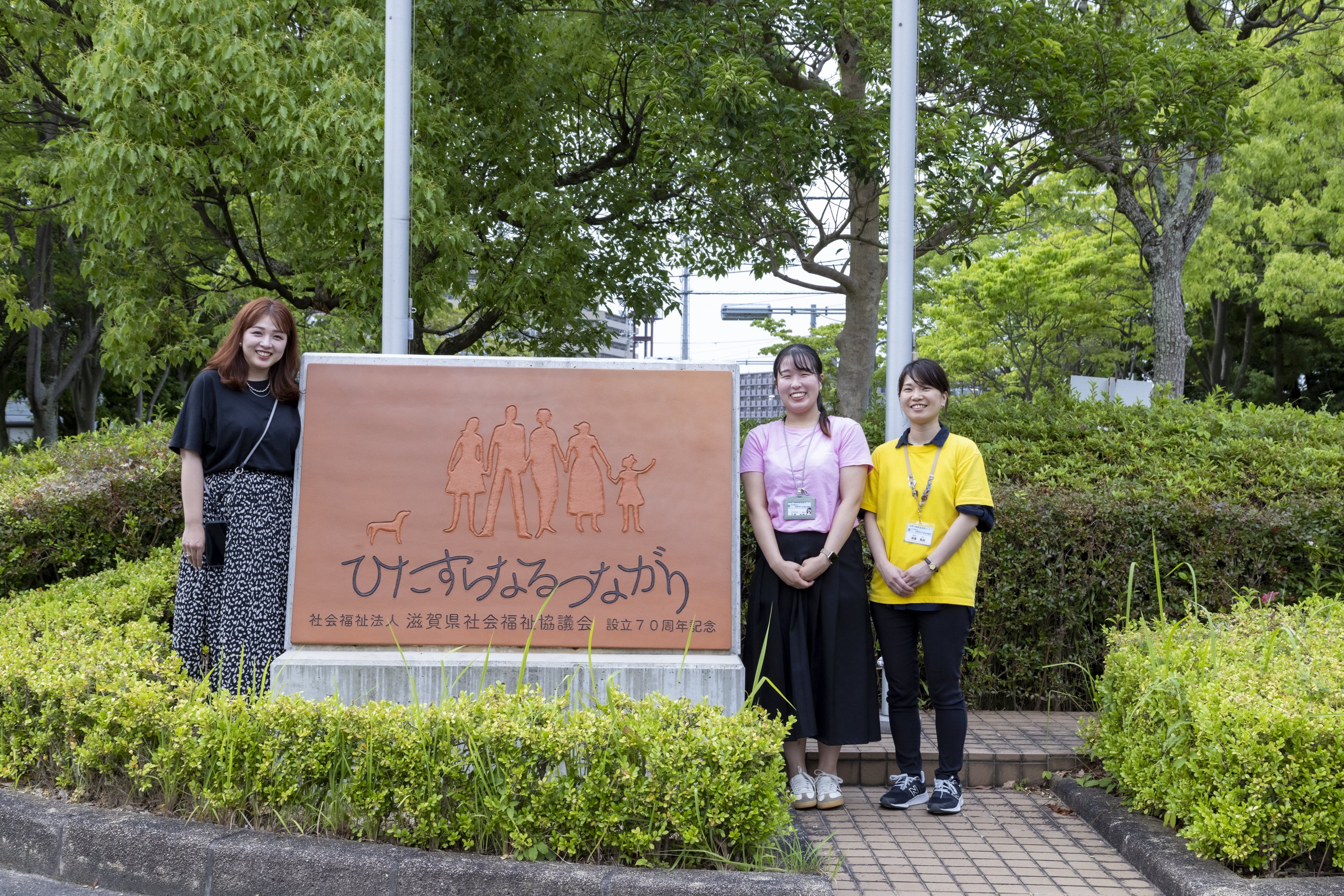 (from left) Ms. Kuwano, Ms. Sannomiya, and Ms. Asaka in front of a monument indicating the corporate philosophy of the Shiga Prefectural Council of Social Welfare. 